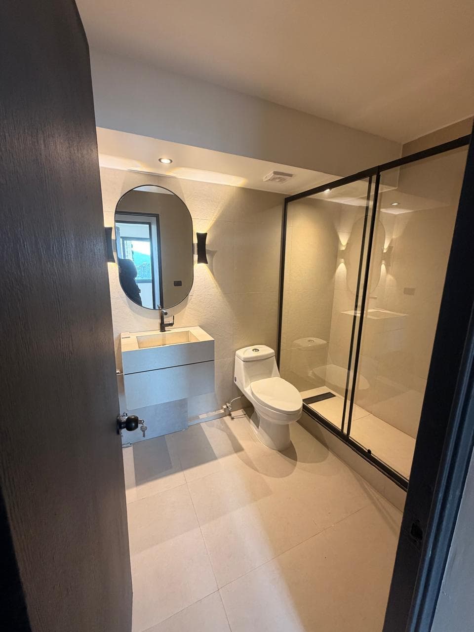 Baño terminado con ducha de vidrio, vanitorio y espejo ovalado