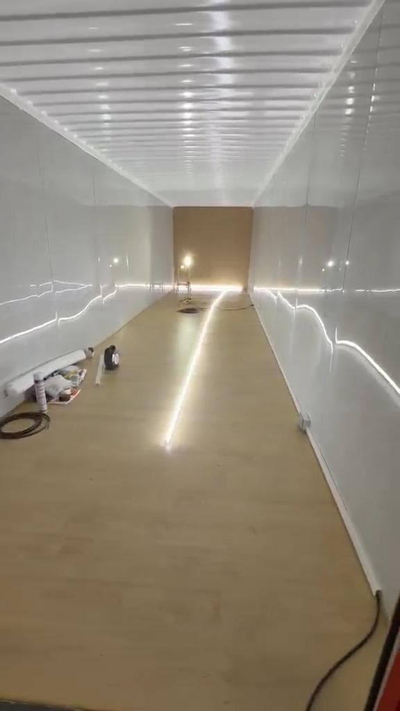 Interior de contenedor revestido en blanco, con piso laminado e iluminación LED