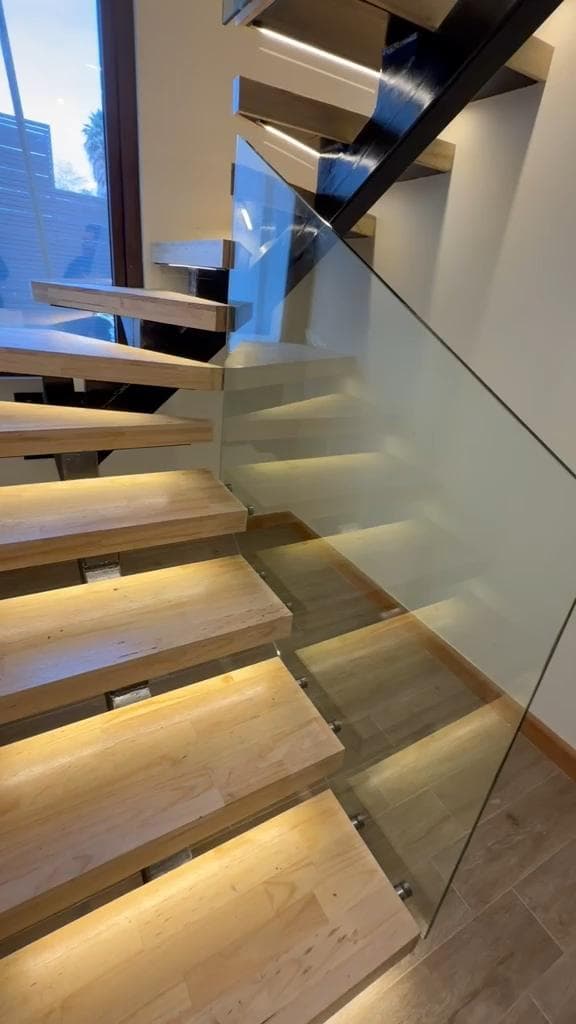 Escalera de madera con baranda de vidrio e iluminación bajo los peldaños
