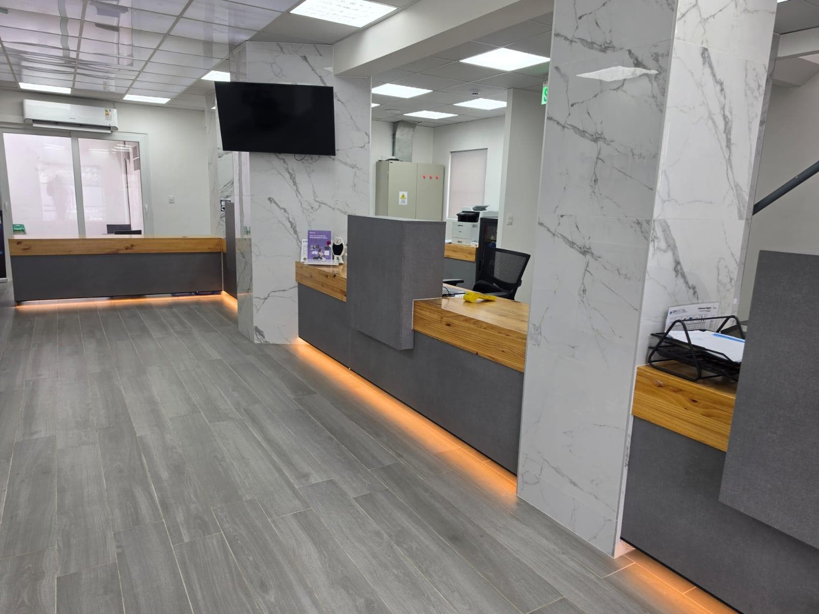 Recepción de oficina terminada, con mesones, revestimiento de mármol e iluminación LED