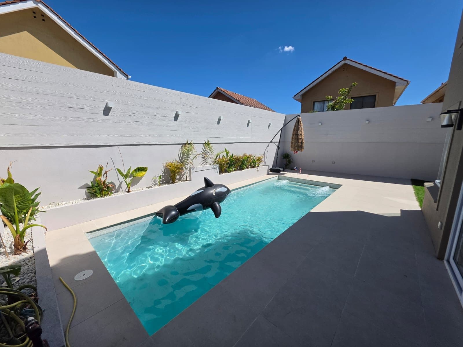 Patio con piscina terminada, terraza de baldosas claras, jardineras y muros perimetrales
